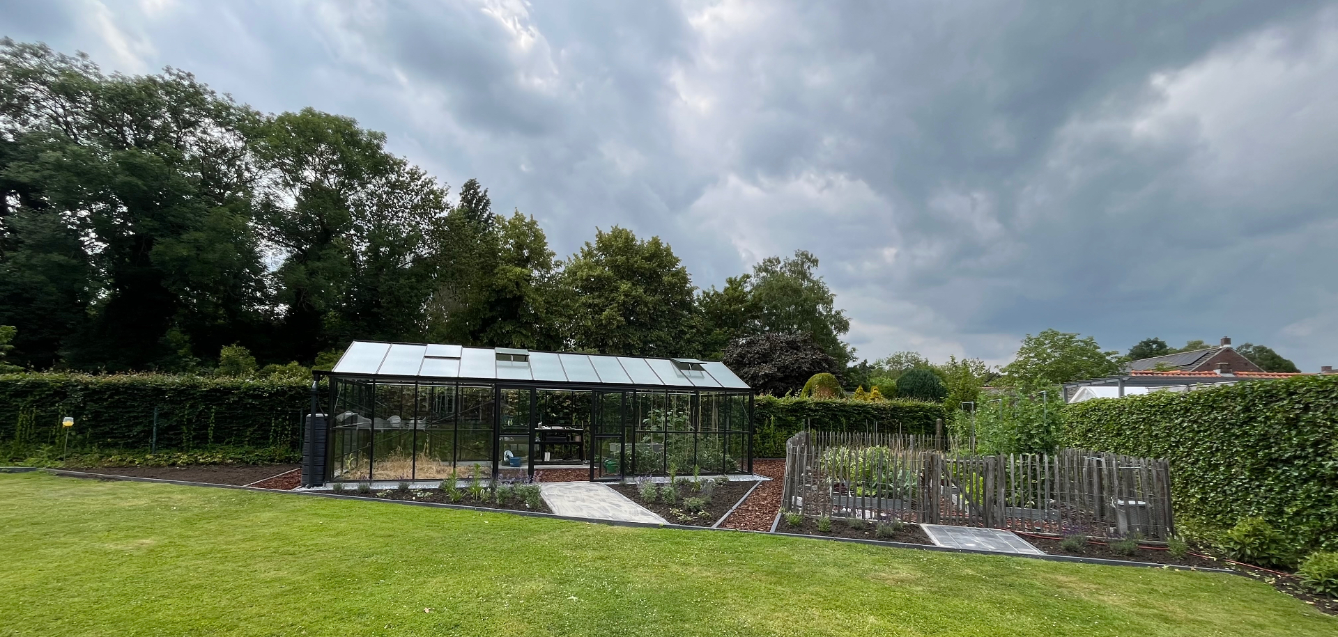 Overzicht van de moestuin met serre en bloemen